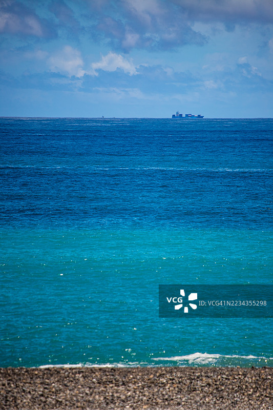 海平线上有货船，前景是卵石海滩和蓝色海洋图片素材
