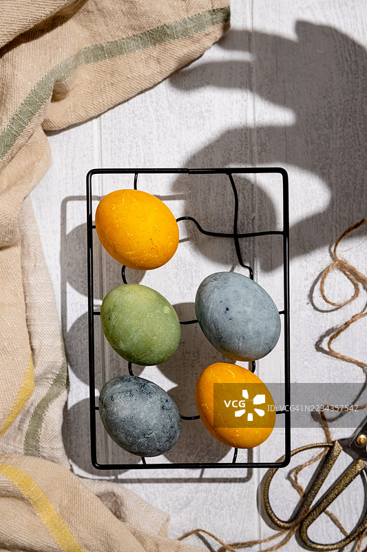 五彩缤纷的染色鸡蛋放在乡村风格的桌子上的铁丝篮中图片素材