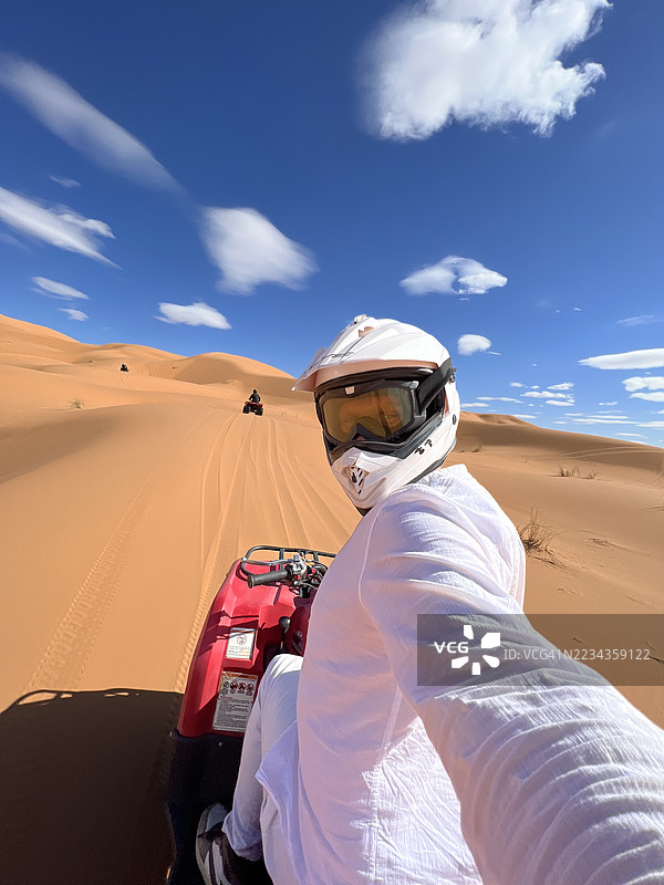 一名男子在摩洛哥撒哈拉沙漠的晴朗蓝天下骑着全地形车图片素材