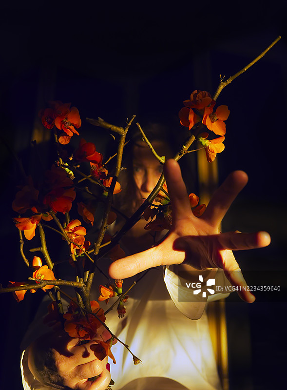 神秘人物伸手穿过开满橙色花朵的树枝图片素材