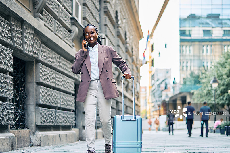 一位女商人在走路时一边打电话一边拉着行李箱图片素材