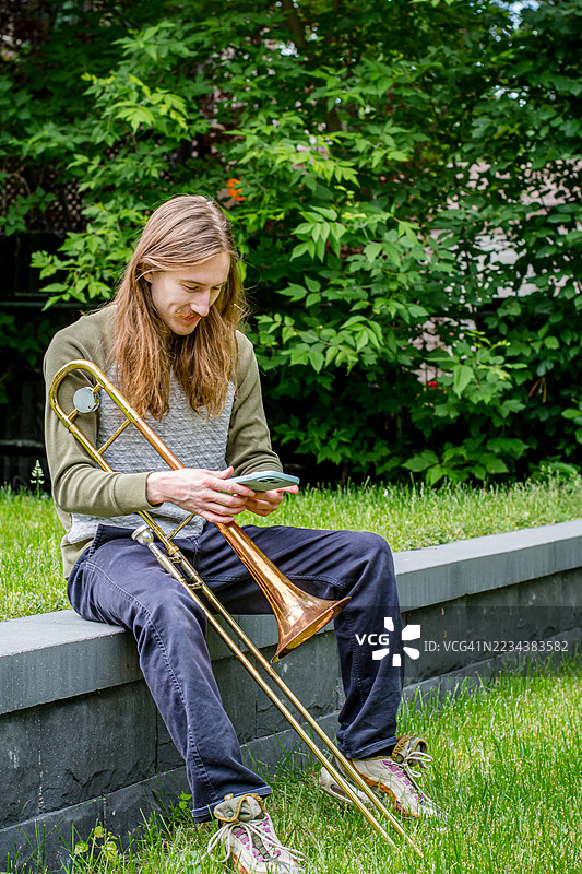 快乐的生活时刻：户外长号演奏者对短信的反应图片素材