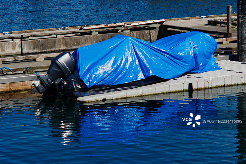 停靠在码头的船上覆盖着蓝色防水布，水面上倒映着船的影子图片素材