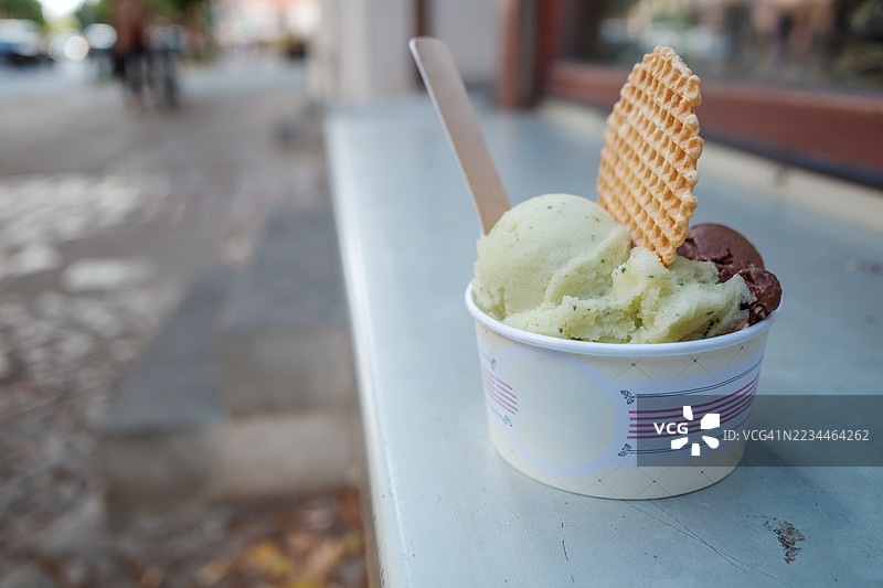 一只手工冰淇淋的纸杯放在城市街道的户外平台上。图片素材