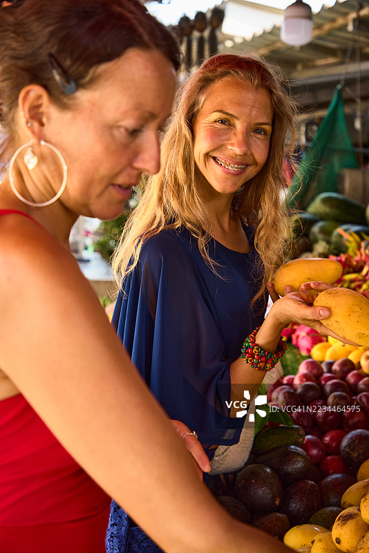 两位女性在热闹的户外水果市场挑选新鲜的芒果图片素材
