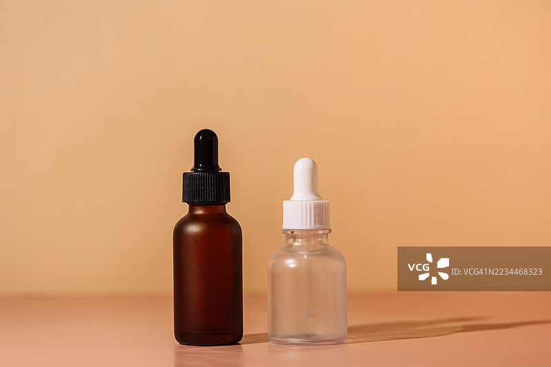 棕色和磨砂玻璃滴管瓶用于护肤产品，放置在桃色表面上图片素材