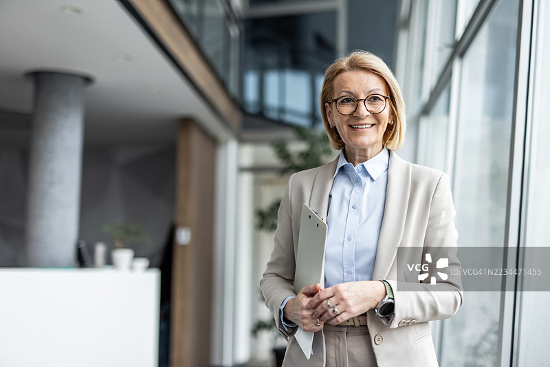 微笑的资深女商人在现代办公室里手持夹板图片素材