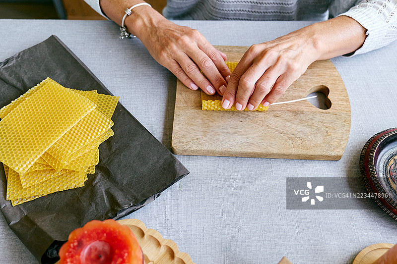 一位无法辨认的女性正在用天然可持续的蜂蜡制作手工蜂蜡蜡烛，蜡烛表面有六角形蜂巢纹理。图片素材