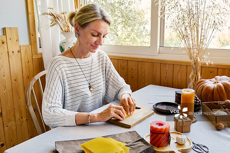 金发女性正在用天然可持续的蜂蜡制作手工蜂蜡蜡烛，蜡烛表面有六角形蜂巢纹理。图片素材