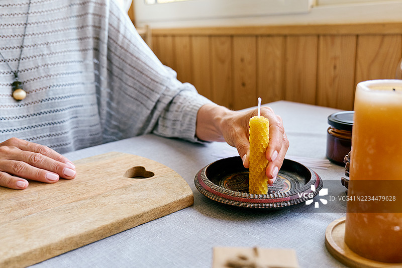 一位无法辨认的女性正在用天然可持续的蜂蜡制作手工蜂蜡蜡烛，蜡烛表面有六角形蜂巢纹理。图片素材