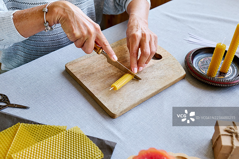 一位无法辨认的女性正在用天然可持续的蜂蜡制作手工蜂蜡蜡烛，蜡烛表面有六角形蜂巢纹理。图片素材