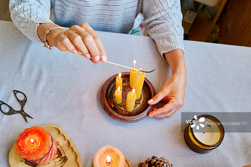 一位无法辨认的女性正在用天然可持续的蜂蜡点燃手工制作的蜂蜡蜡烛，蜡烛表面有六角形蜂巢纹理。图片素材