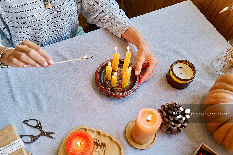 一位无法辨认的女性正在用天然可持续的蜂蜡点燃手工制作的蜂蜡蜡烛，蜡烛表面有六角形蜂巢纹理。图片素材