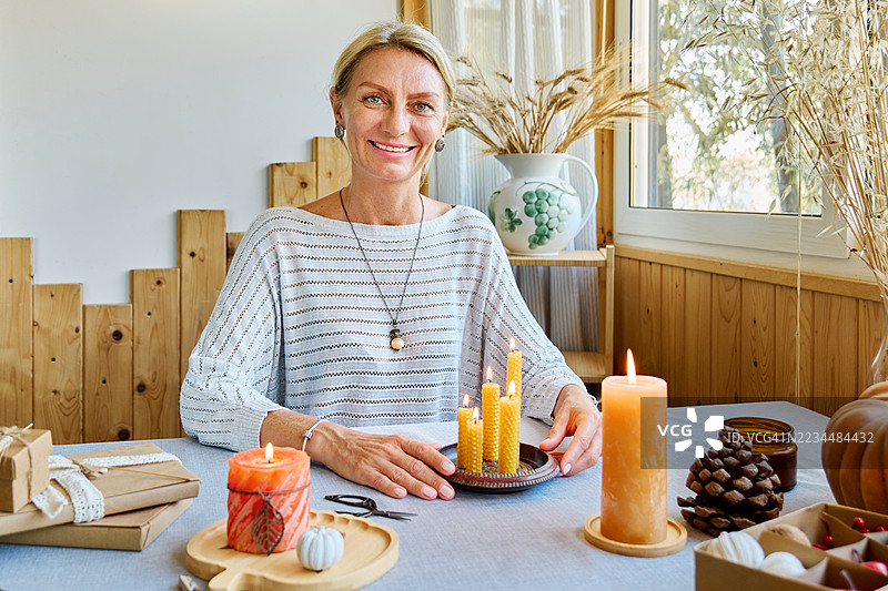 金发女性正在用天然可持续的蜂蜡点燃手工制作的蜂蜡蜡烛，蜡烛表面有六角形蜂巢纹理。图片素材
