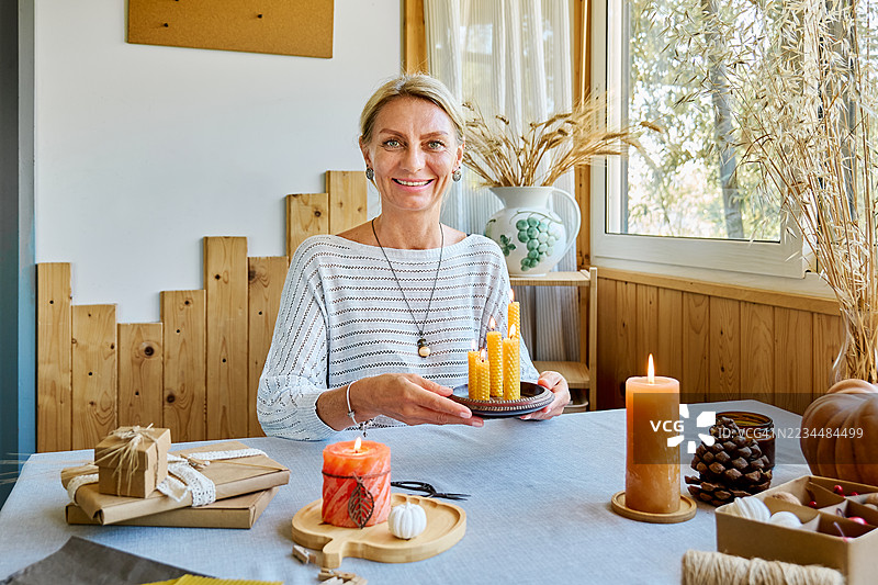 金发女性正在用天然可持续的蜂蜡点燃手工制作的蜂蜡蜡烛，蜡烛表面有六角形蜂巢纹理。图片素材