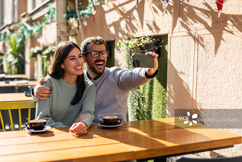 快乐的情侣在户外咖啡馆喝咖啡时自拍图片素材