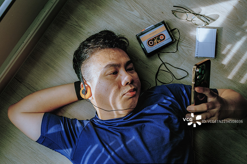 亚洲男子使用智能手机，同时用复古磁带播放器和耳机听音乐图片素材