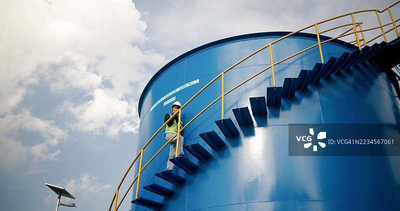 穿着安全防护装备的工业工人或工程师在水处理厂的大型水箱旁工作图片素材