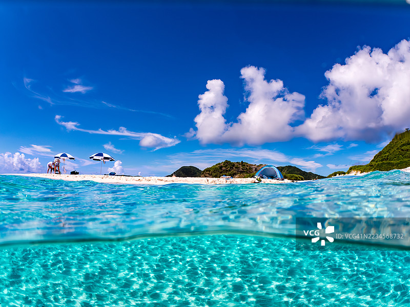 可以看到阳伞、船只，甚至是独特于冲绳的双体船Sabani。拍摄了美丽的白沙滩的一半。还有一群热带鱼。美丽的珊瑚礁和游泳的人们。外岛，座间味岛，慶良間群岛。图片素材