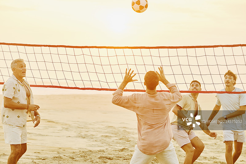 中景拍摄的男人们在友好的沙滩排球比赛中玩耍图片素材