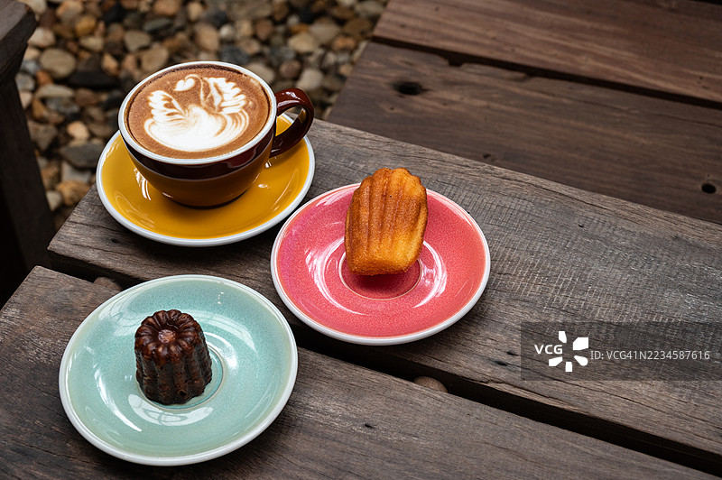 一杯卡布奇诺咖啡配马德琳蛋糕和法式焦糖布丁，摆放在木桌上。图片素材