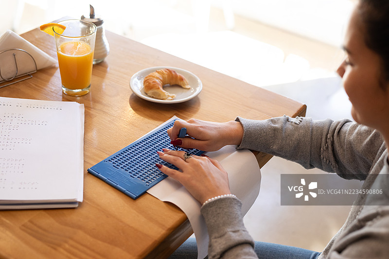 美丽的年轻盲人女性正在使用石板和模板在纸上写盲文。图片素材