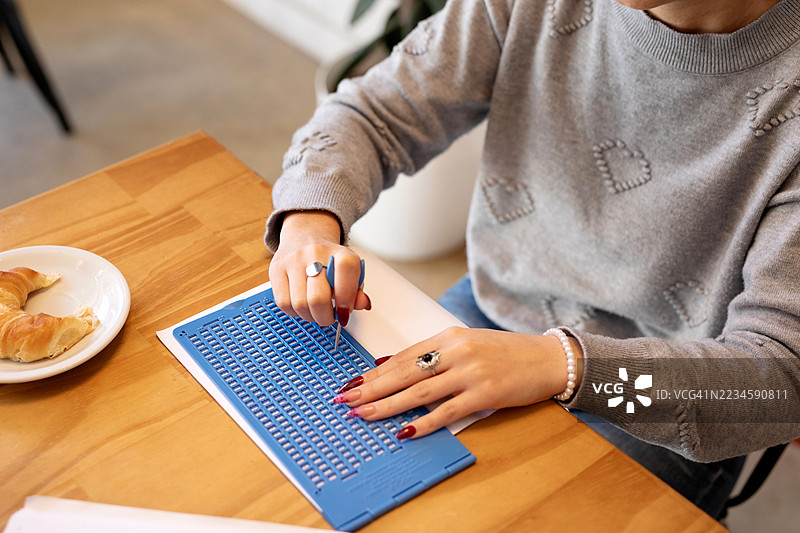 美丽的年轻盲人女性正在使用石板和模板在纸上写盲文。图片素材