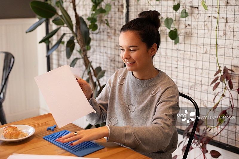 美丽的年轻盲人正在用石板和模板在纸上写盲文。图片素材