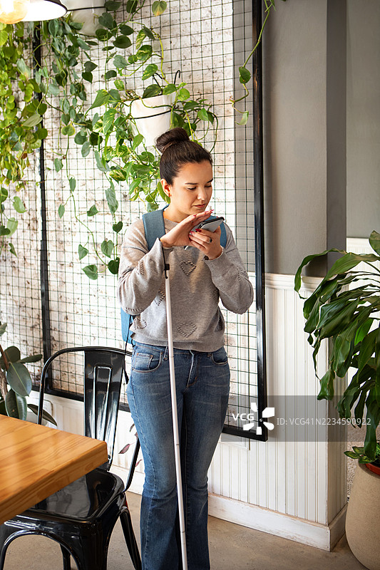 美丽的年轻女性使用带有语音辅助功能的智能手机，帮助视力障碍人士。图片素材