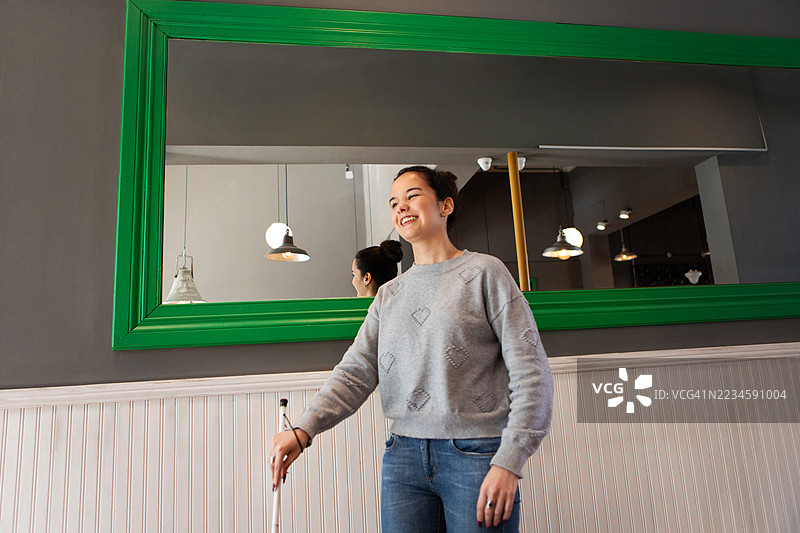 微笑的年轻盲人女性在咖啡馆里用白色手杖行走图片素材