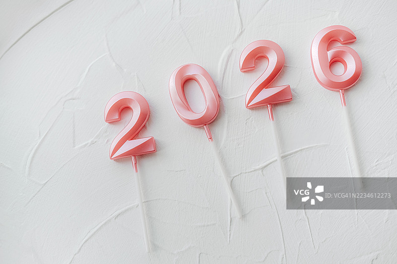 浅粉色数字蜡烛在白色纹理表面上形成2026，插在塑料棒上。图片素材
