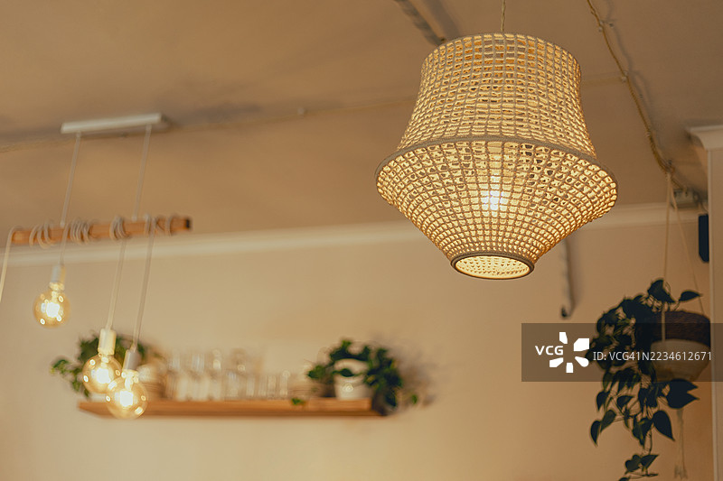 一个编织的吊灯和其他悬挂灯具照亮了一个摆放着盆栽植物的房间。图片素材