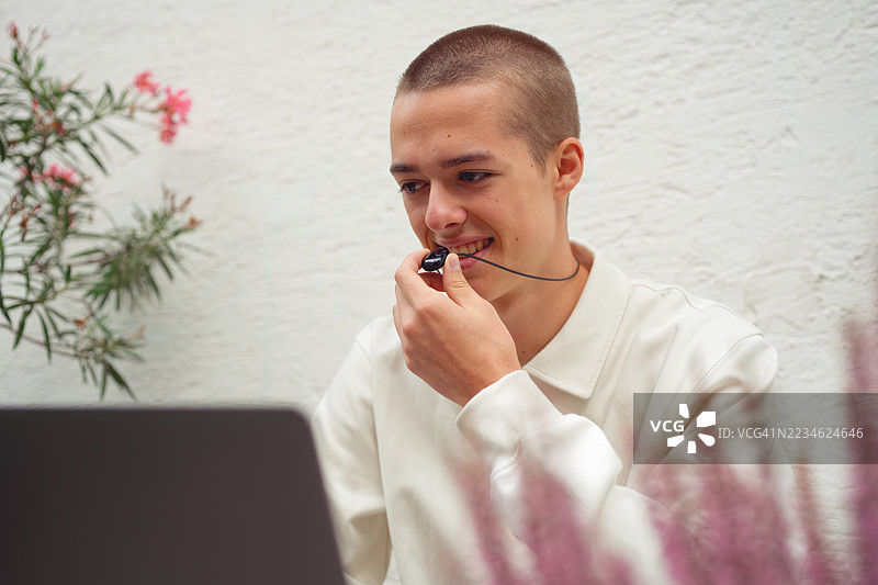 青少年在明亮的户外地点，佩戴着新款人工智能项链，微笑着通过笔记本电脑进行视频通话。图片素材