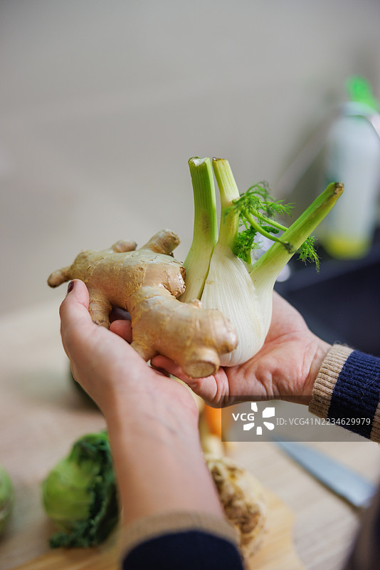 手展示新鲜姜根和茴香球在厨房台面上图片素材
