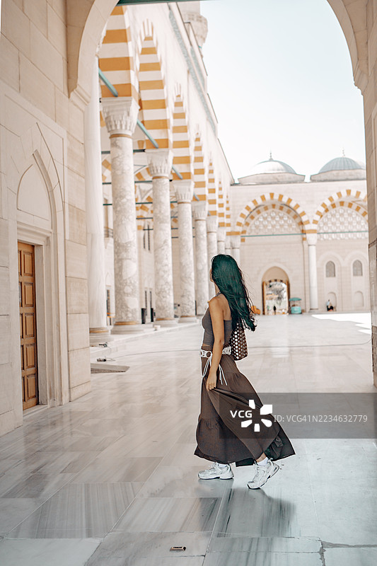 女性游客走过清真寺的内 courtyard，非常适合旅行摄影、文化旅游、建筑欣赏、精神主题和中东生活方式的视觉表现。图片素材