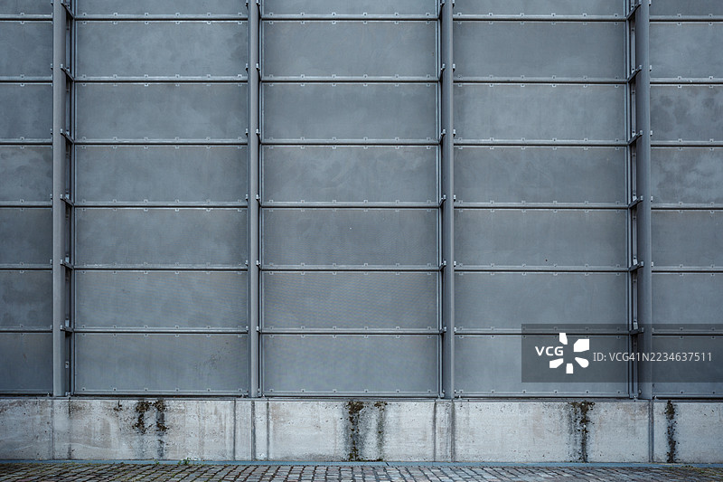 现代金属面板外立面的城市纹理，底部是风化的混凝土，旁边是鹅卵石街道。图片素材