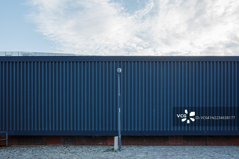 现代波纹金属墙与砖基座和鹅卵石街道。图片素材