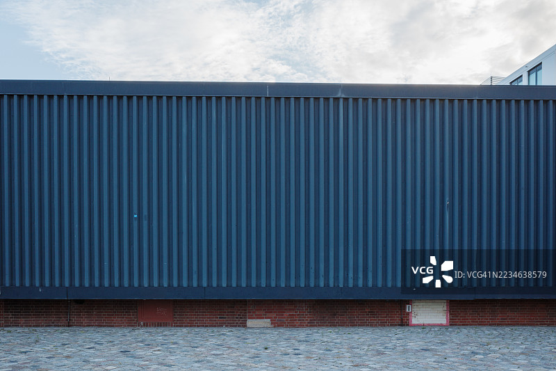 现代波纹金属墙与砖基座和鹅卵石街道。图片素材