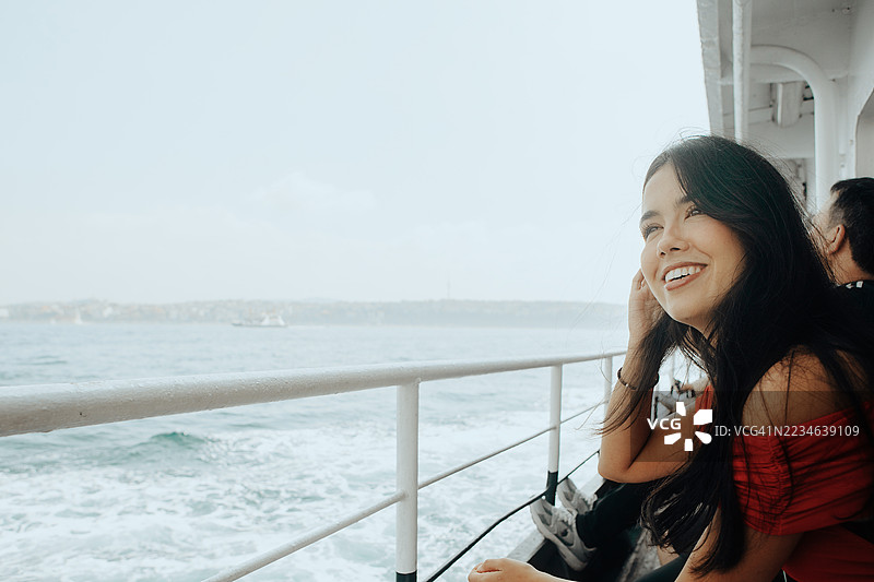 年轻女性在渡轮上欣赏风景，适合旅行摄影、城市风光、旅游、生活方式、冒险、度假和文化探索的视觉效果。图片素材