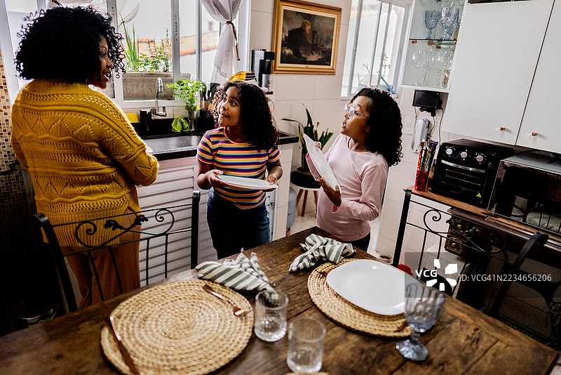 母亲和女儿们在厨房家里布置餐桌图片素材