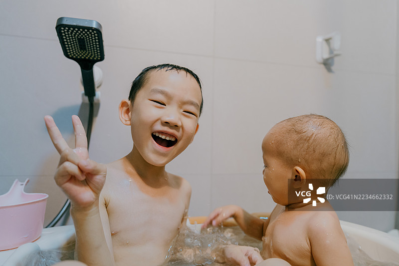 一个亚裔小男孩和他的姐姐在浴缸里洗澡玩耍；亚裔家庭生活方式图片素材