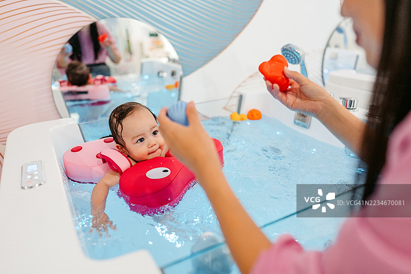 中年母亲在婴儿水疗中心看着她的女儿在浴缸里用浮具游泳图片素材