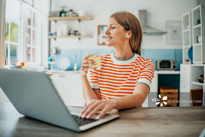 在明亮现代的厨房里享受轻松时刻，手边有笔记本电脑和饮料图片素材