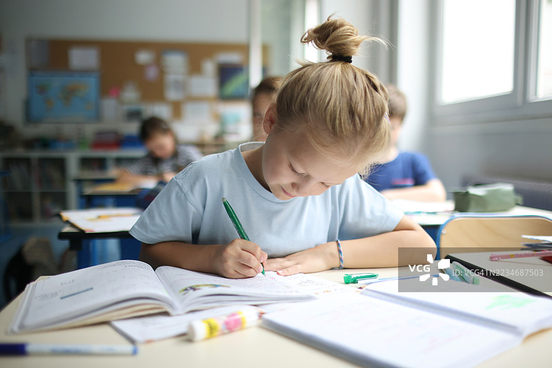 一个小女孩在教室里写笔记本。图片素材