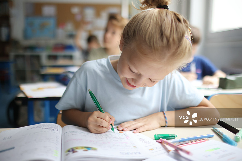 一个小女孩在教室里写笔记本。图片素材