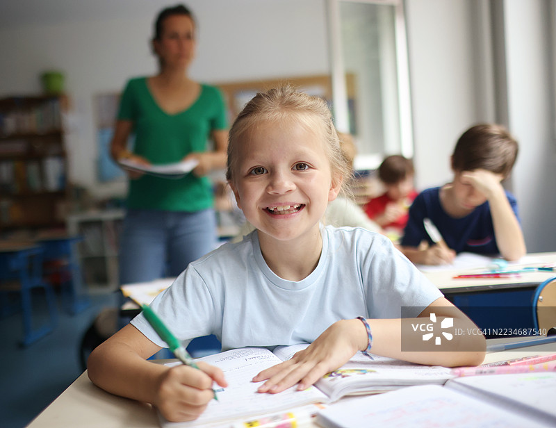 一个小女孩在教室里微笑着写笔记本。图片素材