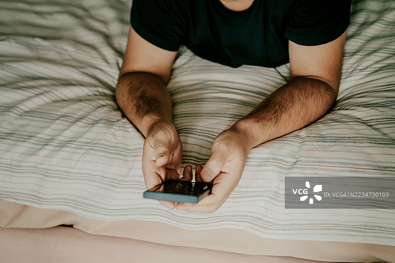 一个人在舒适的条纹床上放松时使用智能手机图片素材
