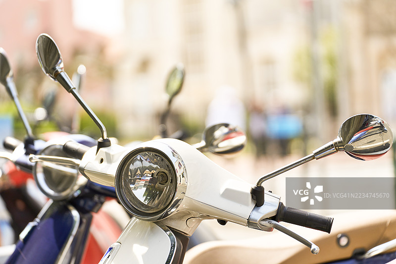 白色滑板车停在城市街道上，镜子中反射出城市生活。图片素材