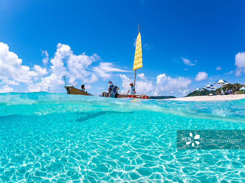 可以看到阳伞、船只，甚至是独特于冲绳的双体船Sabani。拍摄了美丽的白色沙滩的一半。还有一群热带鱼。美丽的珊瑚礁和游泳的人们。外岛，座间味岛，慶良間群岛。图片素材