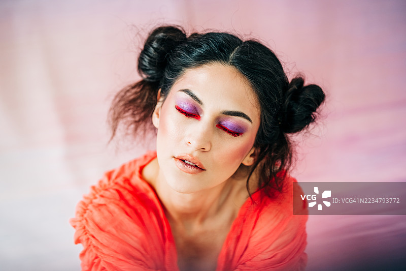 一位年轻女性的特写肖像，拥有鲜艳的红色睫毛和紫色眼妆，面带顽皮的微笑。图片素材